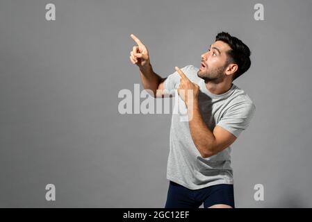 Shocked young Caucasian man with hands pointing up in isolated light gray studio background Stock Photo
