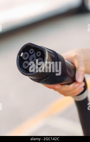 Close-up view of an electric car or EV plug held by a hand in a charging station. Electrical power supply in a power station and Eco-friendly alternat Stock Photo
