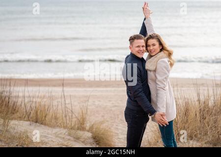 Smiling couple holding hands on the beach.Beautiful young loving couple man and woman hug, holding by hands over his head at evening. Stock Photo