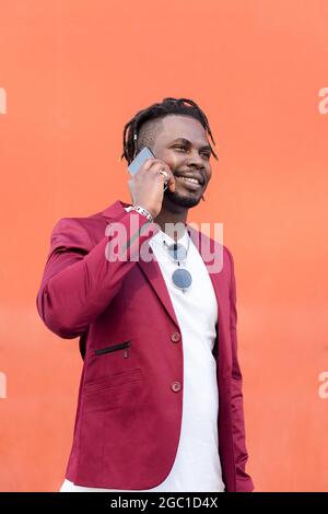 vertical photo of a stylish african businessman in suit smiling and talking on phone in front of red background, copy space for text, concept of techn Stock Photo