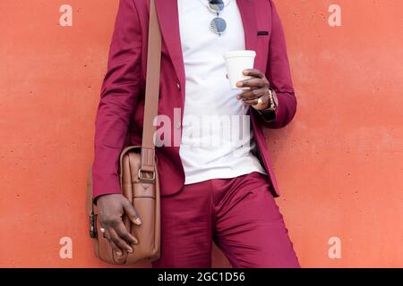unrecognizable stylish african businessman dressed in suit with briefcase holding coffee in his hand in front of red background, copy space for text Stock Photo