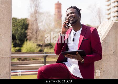 smiling black businessman using a tablet and talking on smart phone outdoors in the city, technology and remote work concept, copy space for text Stock Photo