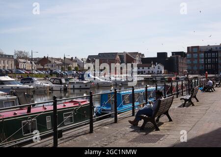 People sat on benches beside Gloucester Quay in Gloucestershire in the UK Stock Photo