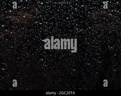 Rain droplets running down on a window glass, abstract backlight background Stock Photo