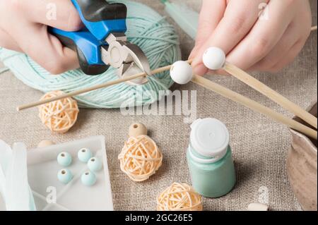 Closeup of female hands cutting wooden stick and mint threads on background. Handmade workshop composition of beads, threads, tools for DIY Stock Photo