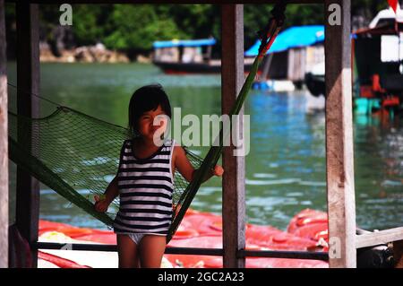 Life and lifestyle of vietnamese girl children people sit playing swing toy at floating fishing village in Halong or Ha Long Bay UNESCO World Natural Stock Photo