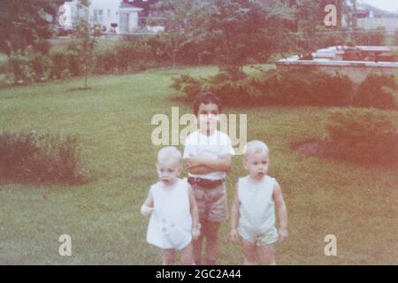 An old photo of three kids standing in the backyard for a photo. Stock Photo