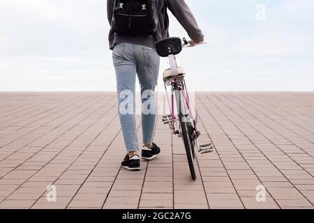 rear view of an unrecognizable young man walking while pushing a bicycle, concept of ecological and sustainable transportation, copy space for text Stock Photo