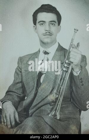 An old photo of a young man posing for a formal portrait while holding his trumpet in his hand. Stock Photo