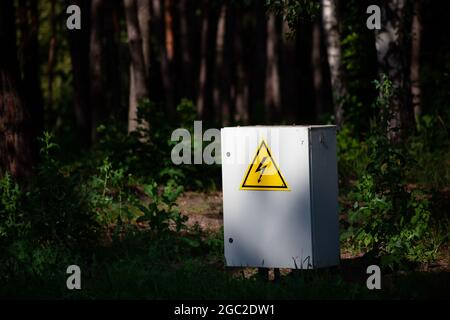 Close up Grey Hinged Power Supply Box in the forest. Outside electrical box with yellow danger warning sign. electricity in remote places. Stock Photo