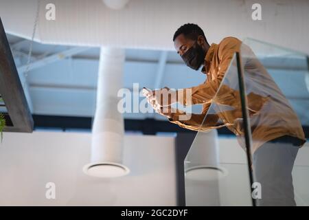 African american businessman wearing face mask and using smartphone Stock Photo
