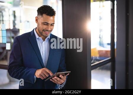 Smiling mixed race businessman using tablet and wearing navy jacket Stock Photo