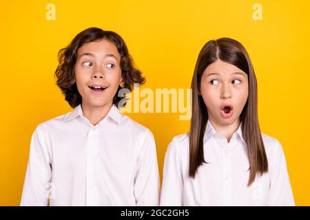 Photo of impressed sweet schoolkids formalwear big eyes looking each other open mouth isolated yellow color background Stock Photo