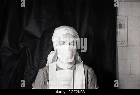 1950s, historical, sitting infront of a black screen, a uniformed nurse wearing a headscarf and a facemask, England, UK. Stock Photo