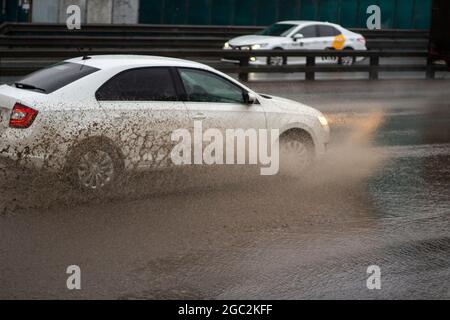 The car is driving through a puddle. Splashes from a puddle on the road. The car, dirty from precipitation, is driving along the highway. A large pudd Stock Photo