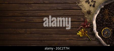 Vintage silver tray with coffee beans, spices and flowers on a table from wooden old textured boards. Banner. Top view. Stock Photo