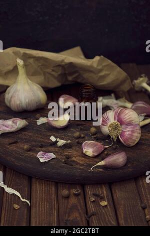 Head and cloves of garlic are scattered on a wooden cutting board on a table made from brown planks Stock Photo