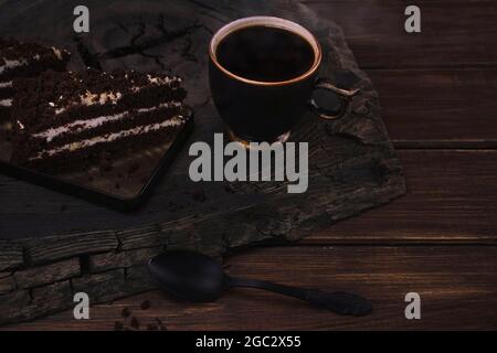 Cup of black coffee with pieces of chocolate cake and spoon on a wooden cracked oak cut. Top view with copy space of brown wooden plank Stock Photo