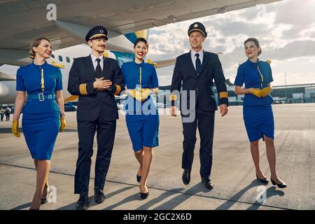 Happy aircrew in uniforms going along the runway Stock Photo