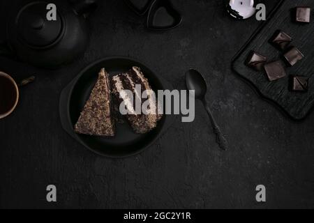 Pieces of cake on a black plate, tea with sweets on a dark background. Flat lay Stock Photo