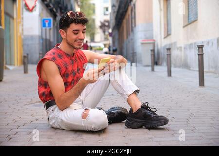 Young caucasian man with long false nails using the phone sitting on floor. Stock Photo