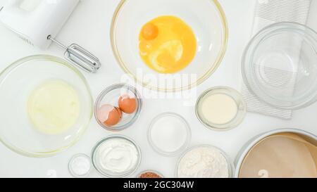 Egg yolks, egg whites, flour, sugar, and some ingredients for cake recipe close up on kitchen table. Homemade chocolate cake step by step baking proce Stock Photo