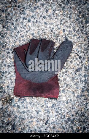 A black and red glove lying on a textured surface in an outdoor setting captures attention Stock Photo