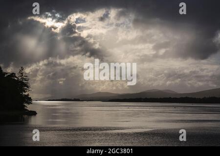 Contre-jour view down Kenmare River in evening light with low sun bursting through cloud with crepuscular rays reflecting on water. Co Kerry Ireland Stock Photo