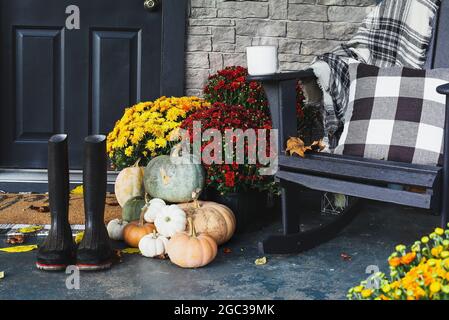 Hot steaming coffee sitting on rocking chair on front porch that has been decorated for autumn with heirloom white, orange, grey pumpkins, rain boots Stock Photo