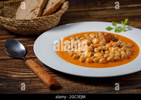 Chickpea stew dish, cocido madrileño. With beef, sausage (chorizo), bacon, carrots and bread. Stock Photo