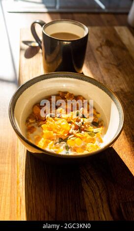 Breakfast cornflakes with seeds and milk and mug of coffee in kitchen Stock Photo