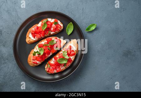 Italian appetizer, bruschetta with tomatoes, cheese and basil on a gray-blue background. Top view, copy space. Stock Photo
