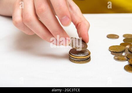 Saving money, a hand puts coins of different countries in a pile, white background, close-up. Stock Photo