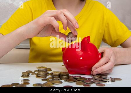 woman hand put money coins in a piggy bank for saving money and financial concept, several coins on the table. Stock Photo