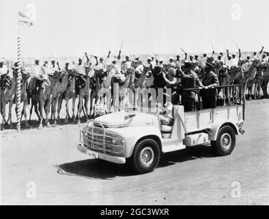 HM Queen Elizabeth II of Britain ( standing in Land Rover ) with her Royal husband , HRH Duke of Edinburgh (left of Queen) and local dignitaries acknowledge cheers , as they drive past during an inspection of the Camel Corps at El Obeid , The Sudan . The Queen flew to the airport here from Khartoum , where she received a great ovation from the locals when she made her Landrover drive around the inner perimeter of the tribal gathering between the lines of camels and tribal dancers . The Queen and the Duke were making a State Visit to the Sudan . The Queen returned to London , and the Duke set o Stock Photo