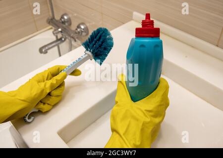 Hands in yellow gloves hold cleaning agent and blue sponge on the handle for cleaning the bathroom. The concept of homework, disinfection Stock Photo