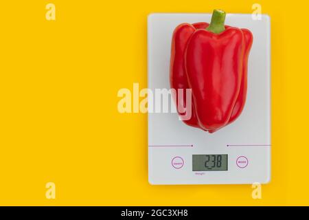 The concept of diet, proper nutrition, healthy eating. Fresh red pepper on a kitchen scale on a yellow background. Weighing products. Top view, copy s Stock Photo