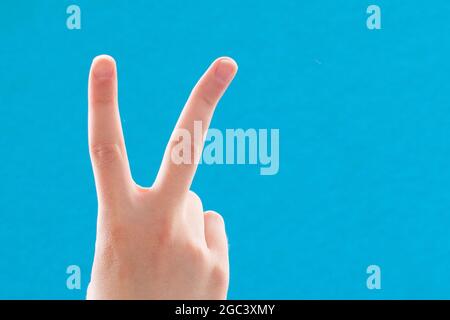 Close-up hand with two fingers up in a symbol of peace or victory. Also a sign for the letter V in sign language. On a blue background. Stock Photo