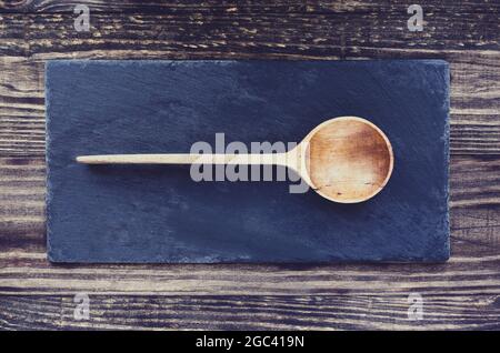 Old antique hand carved wooden spoon with deep bowl made of olive wood over a slate stone and rustic wood table background. Image shot from top view. Stock Photo