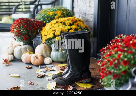 Rain boots sitting on door mat of front porch that has been decorated for  autumn with heirloom white, orange and grey pumpkins and mums Stock Photo -  Alamy