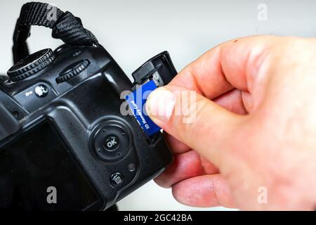 Photographer inserting or removing a blue memory card into the slot in the camera. Data storage and protection. Photographic equipment and technology Stock Photo