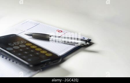 Ballpoint pen on a ring binder with blank pages and a mobile phone with the calculator running. Selective focus. Stock Photo