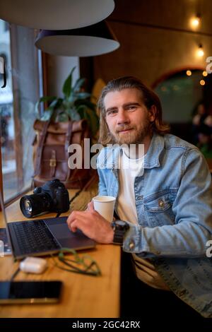 Smiling caucasian male designer working on marketing project at cafe, skilled handsome guy photographer noting ideas earning money on editing images o Stock Photo