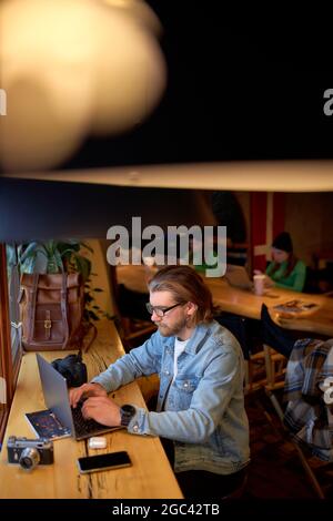 Concentrated on work caucasian male designer working on marketing project at cafe, skilled handsome guy photographer noting ideas earning money on edi Stock Photo