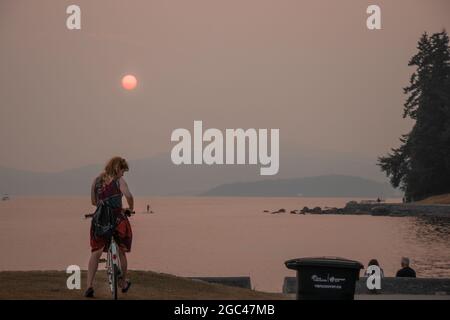 Vancouver, Canada -August 1,2021: Smokey Sky over Vancouver from wildfires. Photo shows the woman standing on a second beach in Stanley Park at sunset Stock Photo