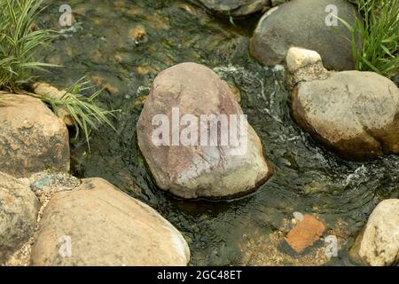Water runs over the stones. Fresh water stream. Artificial waterfall. Landscaping on the territory. Stock Photo