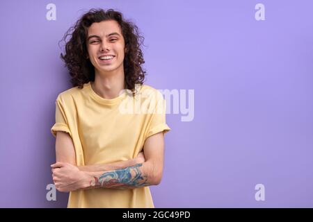 Cheerful Brunette Guy With Long Curly Hair Laughing, Standing With Arms Folded. Man Is In Good Mood, Happy Guy In Casual Wear Enjoys Life Stock Photo