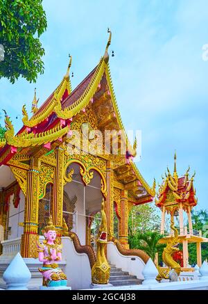 The ornate viharn hall of Wat Sangkharam Temple with pyathat (gable) roof, fine gilt patterns, carved bargeboards, sculptures of Naga serpents and Dev Stock Photo