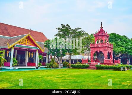 Walk the scenic green garden of Wat Phra That Hariphunchai Temple and watch the old red building of Ho Rakang ceremonial bell tower, Lamphun, Thailand Stock Photo