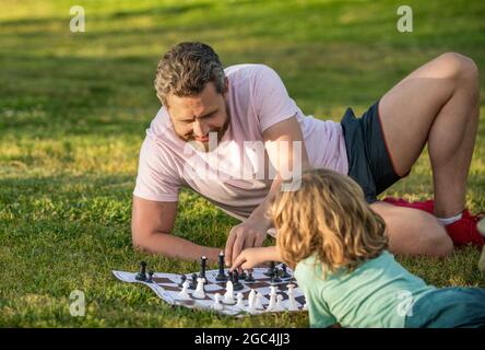 happy family of daddy and son boy playing chess on green grass in park outdoor, chessboard Stock Photo